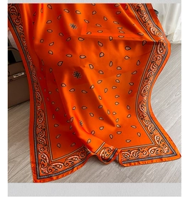 Dettaglio di un foulard in seta arancione con motivi paisley e pois su fondo legno