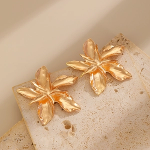 Macro shot of 3D textured gold flower earrings with rippled petals on stone surface