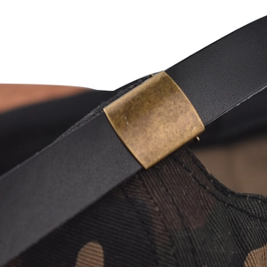 Détail de la sangle réglable en cuir noir avec boucle en bronze sur casquette camouflage