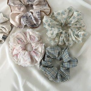 Detailed flat lay of four assorted lace, floral embroidery, and plaid hair scrunchies