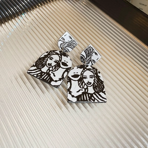 Detail view of pop art earrings with retro face sketches on a ribbed glass tray