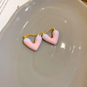 Detail of pink enamel heart-shaped earrings with gold plating on a ceramic tray