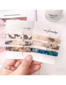 Close-up of three colorful acetate hair clips with amber and marble patterns on card