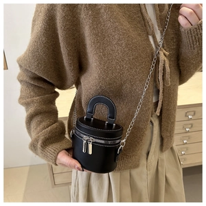 Mini sac cylindrique noir avec bandoulière chaîne argentée porté par un mannequin