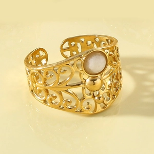 Detail of gold open ring featuring hollow patterns and a white round gemstone