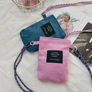Flat lay of corduroy mini crossbody bags in pink and teal with colorful braided straps