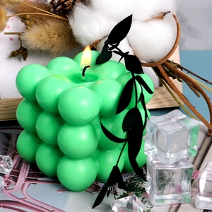 Close-up of a lit green bubble cube candle made from 3D silicone mold on art book