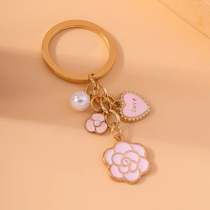 Golden keychain with pink camellia flower, pearl, and love heart charm on warm background