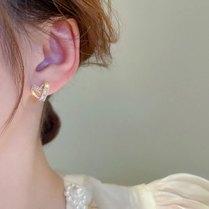 Close-up of gold heart stud earrings with cubic zirconia stones worn by a model