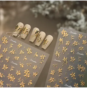 Detail of gold embossed flower nail stickers with 3D floral textures and beige nail tips