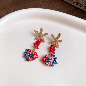 Detail of starfish earrings with red beads and colorful fish pendants in a ceramic tray
