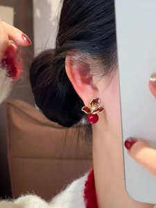 Détail de la boucle d'oreille fleur rouge avec perle et bordure dorée sur modèle