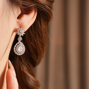 Close-up of elegant flower stud earrings with pink drop pendant on a female model