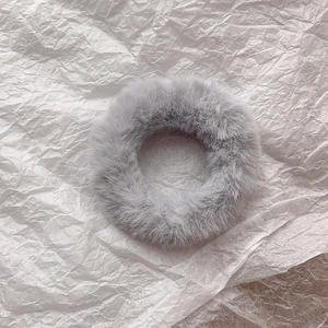 Top view of a fluffy light grey faux fur scrunchie on a white textured paper background