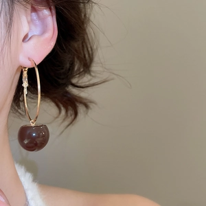 Close-up of a model wearing a gold hoop earring with a dark cherry-like resin ball pendant