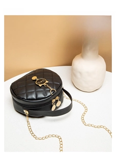 Close-up of black quilted mini bag with gold cat ornament and metal chain strap