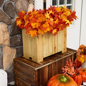 Close-up of artificial maple leaf branches in a rustic wooden planter box for autumn decor