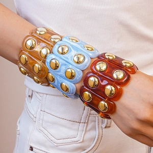 Close-up of chunky resin bangle set with gold dome studs in amber, blue and red