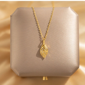 Close-up of golden leaf pendant with white zircons on champagne satin background