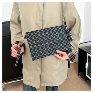 Detail of black envelope clutch featuring white M-letter monogram and wristlet strap