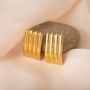 Modern gold-plated ribbed tube earrings displayed on soft silk fabric with a smooth stone