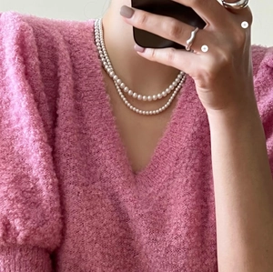 Close-up of double-layer white pearl necklace styled with a pink V-neck knit top