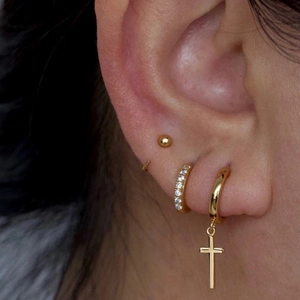 Primer plano de pendientes dorados con cruz y aro con circonitas puesto en la oreja