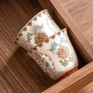Set of two silver enamel ceramic tea cups with Chinese floral patterns on a wooden tray