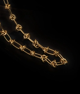 Detailed view of 18K gold knot chain necklace showing polished texture on dark background