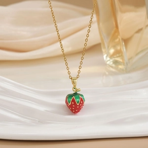 Elegant gold chain necklace with a red strawberry pendant on a minimalist white stand