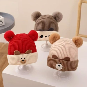 Detail of baby knitted hats with twin pom-poms and cute cartoon bear face design
