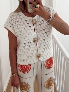 Close-up of golden sun-shaped buttons on a white hollow-out knit short-sleeve cardigan