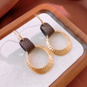 Retro hammered gold ring earrings with brown leather accents on a textured display