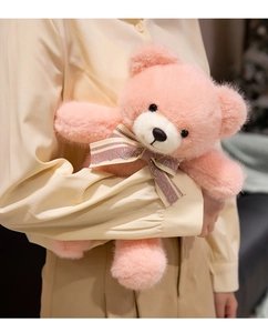 Detail of pink teddy bear plush with LOVE sequined bow held in a warm embrace