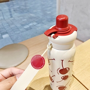 Detail view of cream white thermal bottle with red cherry print and portable strap cord