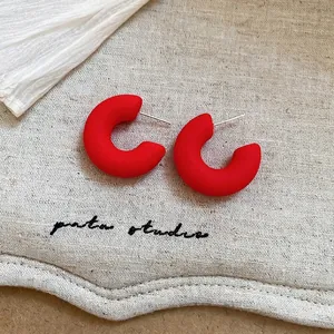 Macro view of matte red C-shape stud earrings with silver pins on a beige linen background