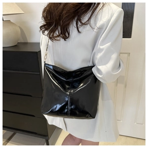 Detail of a black glossy hobo bag with metal chain strap worn over a white blazer
