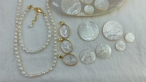 Flat lay of oval white shell pendants with Sacred Heart motifs on beige pleated fabric