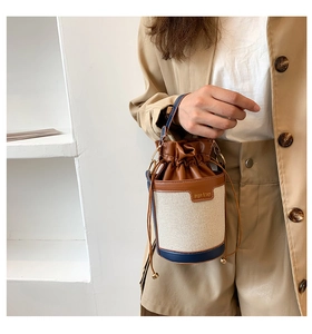 Close-up of canvas bucket bag with leather trim, drawstring closure and metal handle