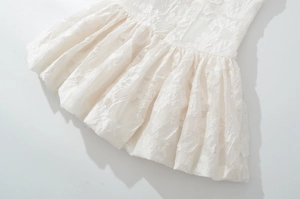 Close-up of white floral lace fabric and pleated hem detail on a mini camisole dress