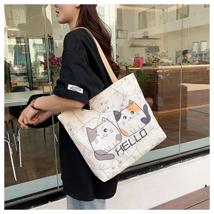 Detailed view of cream canvas tote bag featuring a cartoon cat print and Hello text