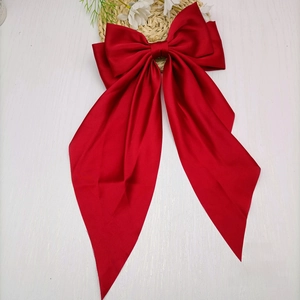 Macro shot of silk red bow hair clip with long ribbons on a white wooden table