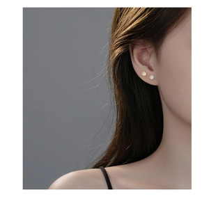 Close-up of minimalist sun earrings in gold and silver colors worn by a model