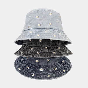 Detailed close-up of daisy floral embroidery on stacked denim bucket hats in three colors