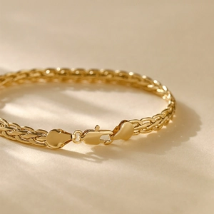 Macro detail of 14K gold plated braided chain bracelet with a secure lobster clasp closure
