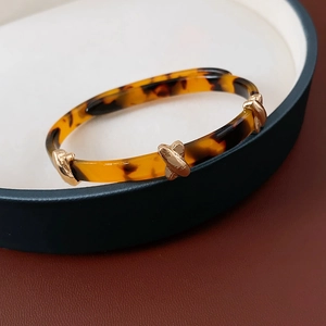 Detail of leopard resin cuff featuring a golden X-shaped metal decorative hardware