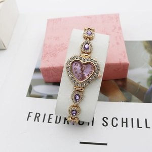 Détail d'une montre à quartz violette en forme de cœur avec bracelet doré et strass brillants