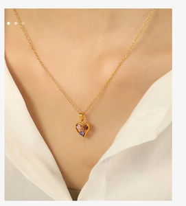 Detail of gold heart pendant necklace featuring three colorful inlaid gemstones on a model
