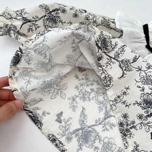 Close-up of baby girl top with vintage floral print, black bow and ruffle collar detail