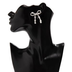 Detailed view of elegant white pearl bow earrings on a black display bust